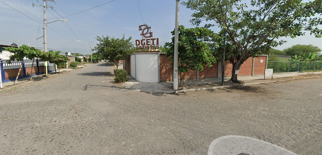 Fotografía en la que se muestra la entrada del plantel, conformada por una puerta color blanco y arriba de ella, en letras grandes rojas dice Degeti y Cebetis 285. El plantel se ubica en la esquina de la calle.